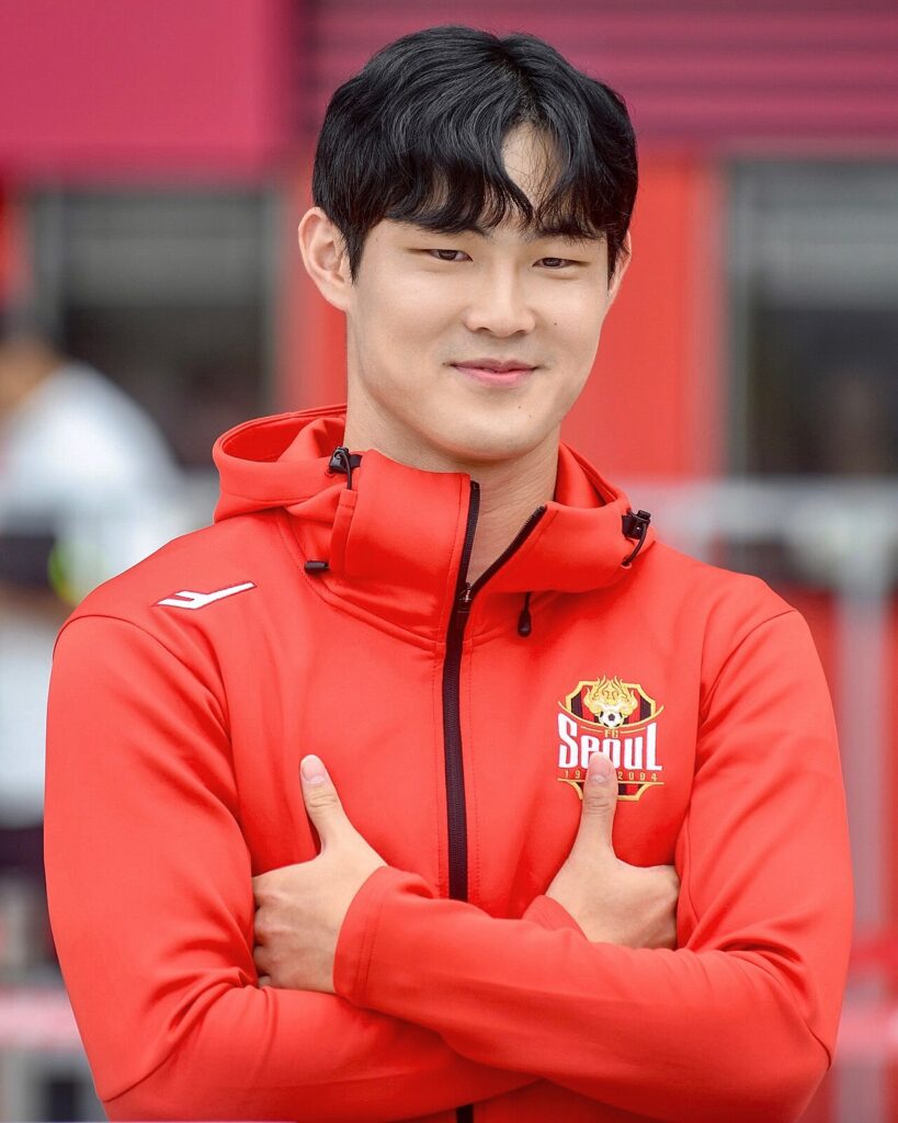 FC 서울 엠블럼이 있는 빨간 재킷을 입고 팔짱을 낀 강성진